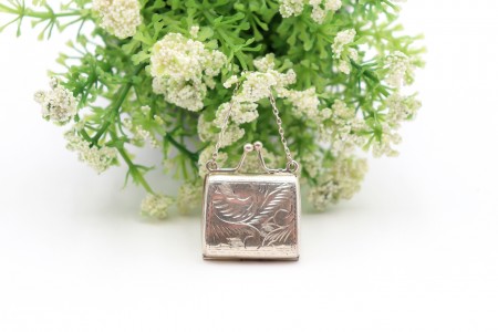 Caixa de comprimidos em prata em forma de mala com gravados e corrente